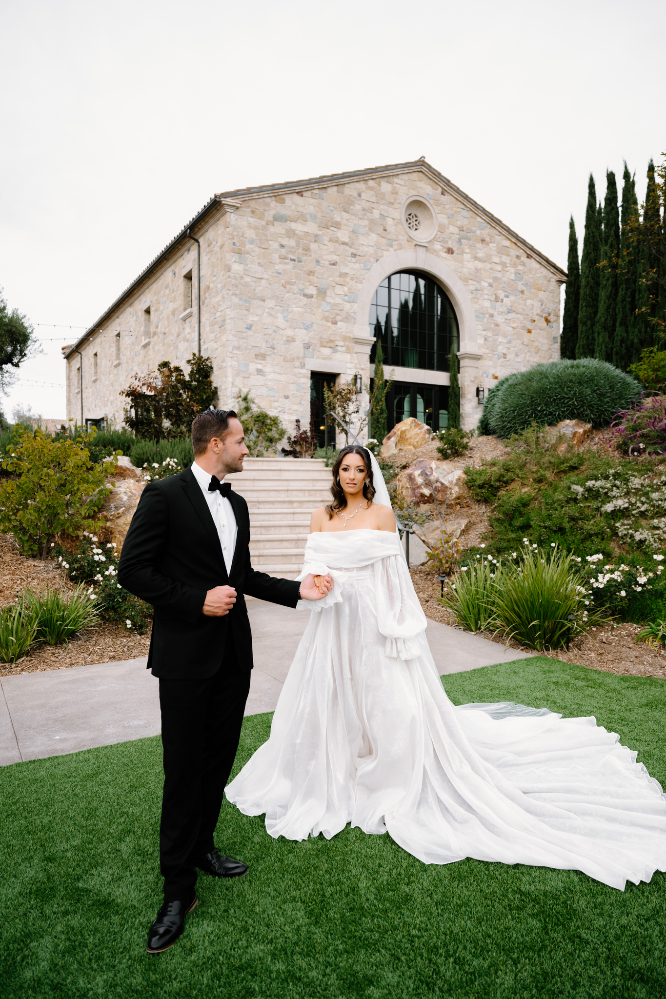 Couple holding hands, a couple steps apart from each other, at a beautiful winery.